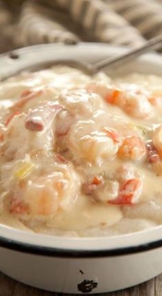 a white bowl filled with shrimp and grits on top of a wooden table next to a fork