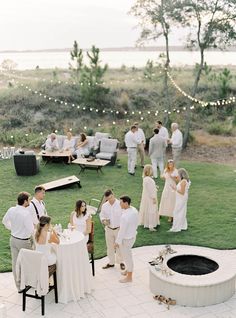 a group of people standing around a fire pit on top of a lush green field