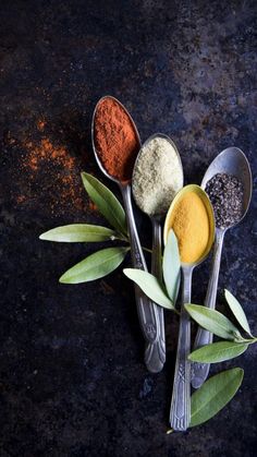 three spoons filled with different types of spices on top of a black countertop