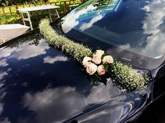 flowers are placed on the hood of a black car with clouds in the sky behind it