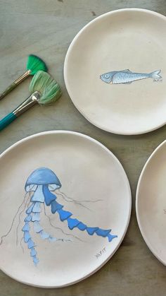 three plates with drawings on them sitting on a table next to paintbrushes and brushes