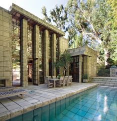 an outdoor swimming pool with chairs and tables next to the side of the house that is surrounded by trees