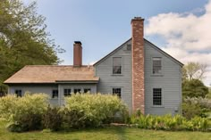 a gray house sitting in the middle of a lush green field