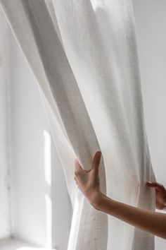 a person is opening the curtains with their hand to look at something in the distance