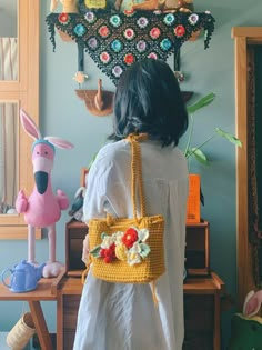 a woman holding a yellow crocheted purse next to a stuffed animal and other items