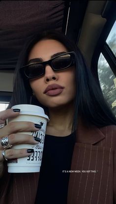 a woman wearing sunglasses and holding a coffee cup in her hand while sitting in a car