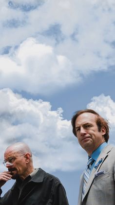 two men standing next to each other under a cloudy sky with clouds in the background