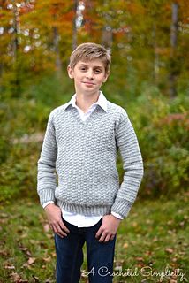 a young boy is standing in the woods wearing a sweater and jeans with his hands on his hips