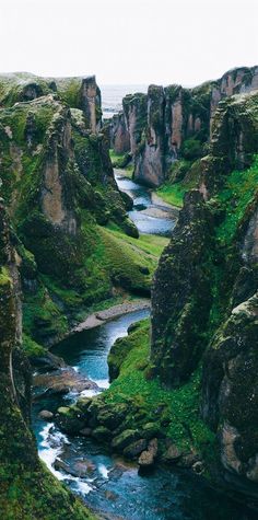 a river flowing through a lush green valley next to tall rocky cliffs covered in grass