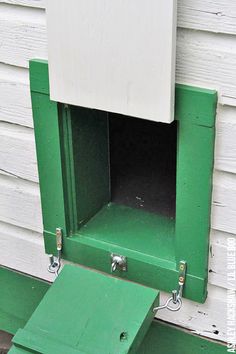 a green and white bird house sitting on the side of a building with its door open