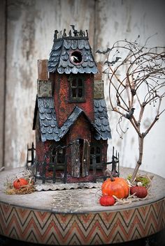 a doll house sitting on top of a table next to a tree and pumpkins