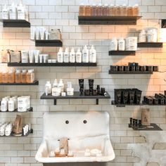 a white sink sitting next to shelves filled with lots of bottles and containers on the wall