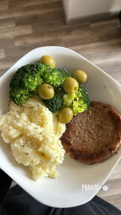 a white plate topped with meat, mashed potatoes and broccoli covered in olives