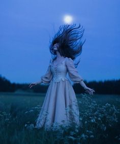 a woman in a white dress standing in a field with her hair blowing in the wind