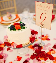 a white cake with red and orange flowers on it sitting on top of a table