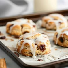 cinnamon rolls with icing and raisins sitting on a baking tray next to cinnamon sticks