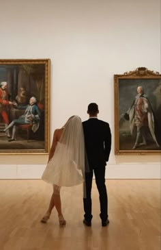 a bride and groom looking at paintings in an art gallery