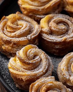 several pastries on a black plate with powdered sugar and cinnamon swirl toppings