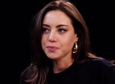 a close up of a person wearing gold earrings and a black shirt with long hair