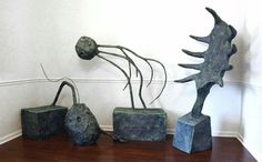 three metal sculptures on top of a wooden table next to a white wall and wood floor