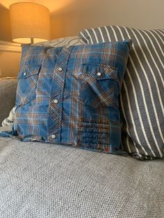 a blue plaid pillow sitting on top of a gray couch next to a striped lamp