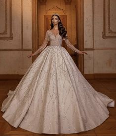 a woman in a ball gown with long sleeves and beading on the skirt is standing in front of a doorway