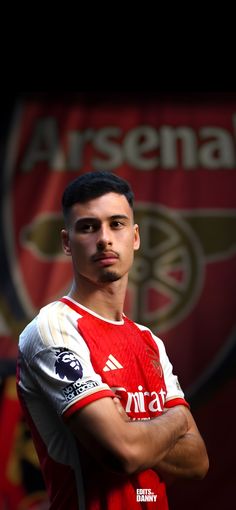 a soccer player with his arms crossed in front of a sign that reads arsensa