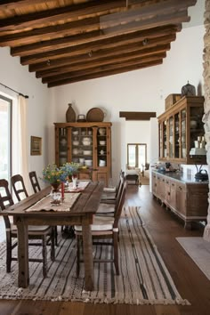 a dining room table and chairs in front of an open kitchen with wood beams on the ceiling