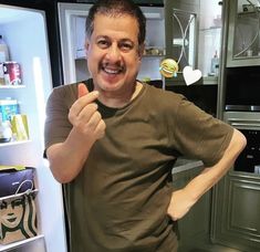 a man standing in front of an open refrigerator with his hand on the door and smiling