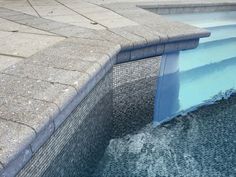 an empty swimming pool with blue water and stone steps leading up to the side wall