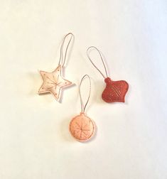 three ornaments are hanging from strings on a white surface, one is shaped like a star and the other has an ornament in the shape of a fish