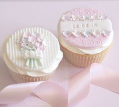 two decorated cupcakes sitting next to each other on a pink surface with a ribbon