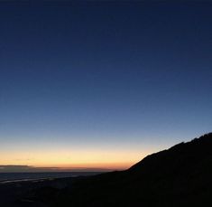 the sun is setting at the top of a hill with a view of the ocean and mountains in the distance