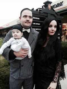 a man and woman are dressed up for halloween with a baby in their arms while standing next to each other