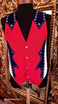 "This patriotic western vest is from the 90's and was custom made for the original owner. Beautifully made. The front is a cherry red heavy cotton with navy blue accents.  Snap closure.  Silver studs around the edges and on the shoulder.  The sides are testured white faux leather. Inside the back is a metallic copper stripe.  The outside of the back is a solid black with slide buckle belt. Please see the measurements below for a proper fit.  All sales are final. Measurements Armpit-armpit doubled 40\" Waist 39\" Length 25\" from the center Length 27\" to the points" Fitted Retro Vest For Festivals, Retro Red Cotton Vest, Red Retro Cotton Vest, Red Cotton Retro Vest, Fitted Retro Red Vest, Retro Red Fitted Vest, Fitted Red Retro Vest, Western Vest, Metallic Copper