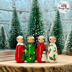 three wooden dolls are standing next to each other in front of a christmas scene with trees