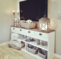 a tv mounted on top of a wooden shelf next to a white cabinet filled with baskets and candles