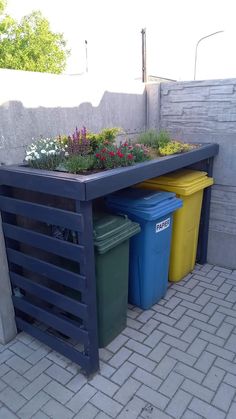 three trash cans sitting next to each other in front of a planter filled with flowers