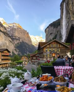 a table with food on it in front of some mountains and people sitting at tables