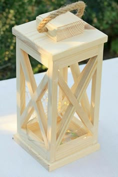 a small wooden lantern sitting on top of a white cloth covered table next to trees