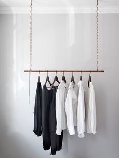 clothes hanging on a rail in front of a white wall and wooden bar with hooks