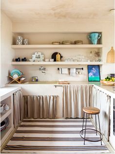 a kitchen with white walls and shelves filled with dishes on top of the counter tops