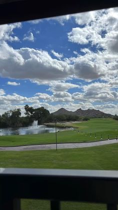 the view from inside a window looking out onto a golf course and lake with mountains in the background