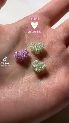 three tiny beads are in the palm of someone's hand, one is purple and one is green