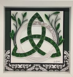 an intricate paper art piece with green and white designs in a frame on the wall