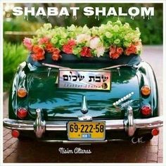 an old green car with flowers in the trunk and writing shabat shalohm