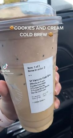 a person holding up a cup of ice cream in their hand with the words cookies and cream cold brew written on it