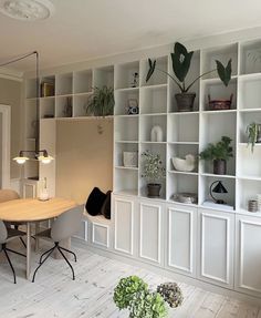 a dining room table and chairs in front of a bookcase with plants on it