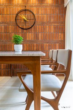 a wooden table with white chairs and a clock on the wall behind it in a room