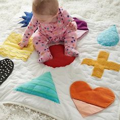 a baby sitting on top of a white rug with lots of different shapes and sizes